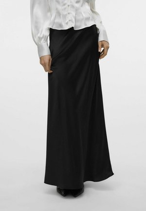 Zwarte, lange rok van gladde stof met een wikkeldesign. G gedragen met een witte blouse met knopen en zwarte schoenen.