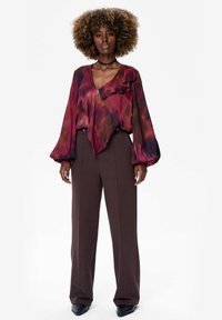 Vloeiende blouse in een rode en bruine gradient met een geschulpte halslijn en lange mouwen, gecombineerd met hooggerokte, bruine pantalon en elegante zwarte hakken.