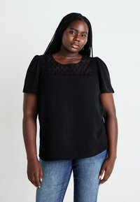 Black short-sleeve top with textured lace yoke. Soft, lightweight fabric with a relaxed fit. Paired with medium-wash denim jeans.