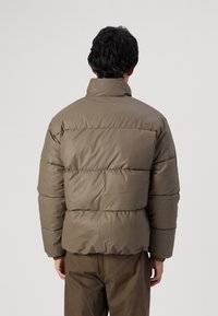 Pufferjakke i olivengrøn, med høj krave, quiltet design og elastiske manchetter. Glat, vandafvisende materiale med en boxy pasform.