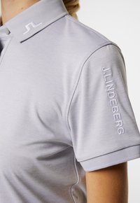 Ljusgrå pikétröja med klassisk krage, med broderad logga på kragen och ärmen. Slät textur, korta ärmar, skräddarsydd passform.