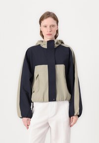 Veste courte en design bicolore bleu marine et khaki. Dotée d'une capuche, d'une fermeture éclair frontale et de poignets élastiques. Texture lisse avec une coupe décontractée.