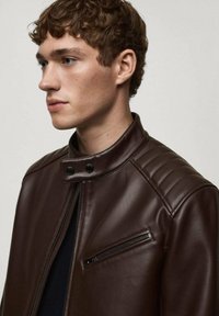 Veste de moto en cuir synthétique marron avec un col haut, une poche zippée et des épaules matelassées. Texture lisse, design élégant.