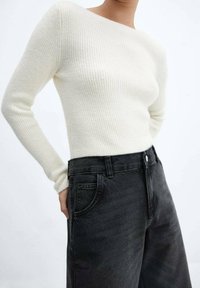 Vanhanvalkoinen ribbineulottu neulepaita pitkillä hihoilla yhdistettynä korkeavyötäröisiin mustiin farkkuihin, joissa on edessä napitus ja taskudetaljit.