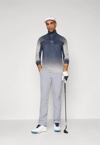 Conjunto de golf para hombre que incluye un polo de manga larga con degradado en azul y gris, pantalones gris claro, zapatos blancos con detalles azules y gorra blanca.