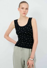 Svart ärmlös topp med rund halsringning, prydd med fina vita prickar, tillsammans med ljusgrå byxor och ett silverarm band.