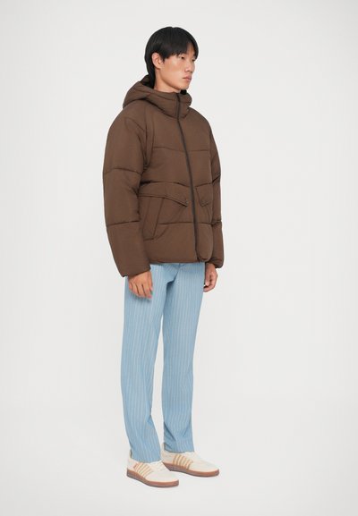 Giubbotto imbottito marrone con cappuccio e zip sul davanti, dotato di due grandi tasche. Abbinato a pantaloni a righe sottili blu chiaro e sneakers bianche.