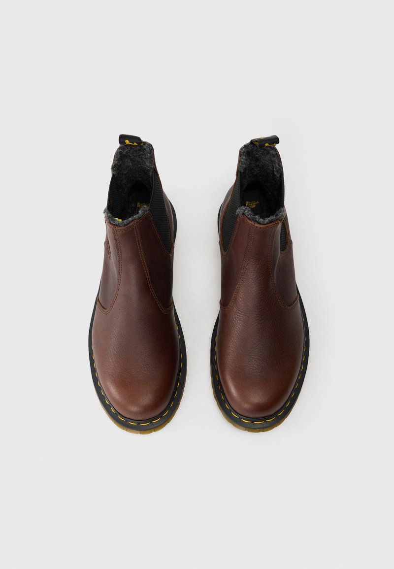 Braune Leder-Stiefeletten mit strukturierter Oberfläche, elastischen Seitenpaneelen, grauem Fleece-Futter und schwarzen Gummisohlen mit gelben Nähten.
