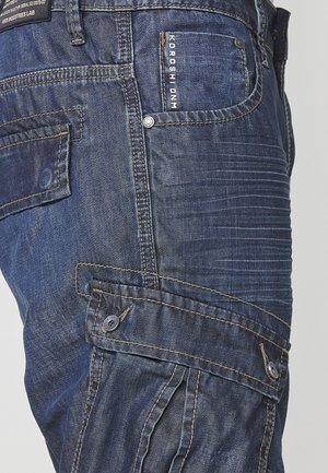Dunkelblaue Denim-Cargo-Hose mit mehreren Taschen, sichtbaren Nähdetails und einer strukturierten Oberfläche. Mit Knopf-Akzenten und Etiketten.