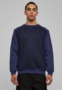 Marineblauwe trui met ronde hals, raglanmouwen en geribbelde manchetten. Gemaakt van een zachte, duurzame stof met een gladde textuur.