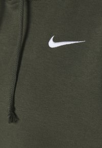 Olivgrön bomullsbyxor med en vit broderad Nike-logotyp. Har dragsko med flätad textur och knutdetaljer.