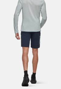 Långärmad ljusblå topp med strukturerad tyg, matchad med marinblå shorts med vit branding och svarta sportskor.