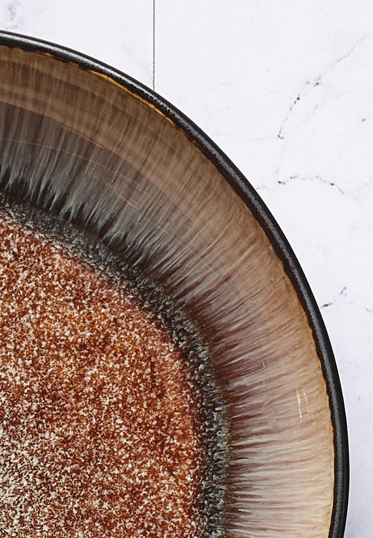 Runder Keramikteller mit einem strukturierten, braunen Innenbereich und einem Rand, der von Dunkelbraun zu Hellbraun übergeht. Glänzende Oberfläche, leicht schimmernd.