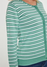 Zeleno-bílý pruhovaný cardigan s kulatým výstřihem, zapínáním na knoflíky vpředu a ribbed lemem. Vyrobeno z měkké, lehké látky.