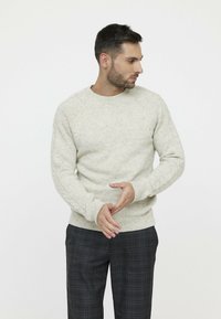 Hellgrau gestrickter Pullover mit strukturiertem Muster, gerippten Bündchen und Rundhalsausschnitt. Getragen mit dunklen karrierten Hosen. Warmer, lässiger Schnitt.