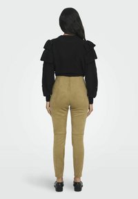 Pull noir court avec des accents de manches froncées associé à un pantalon taille haute en suède beige, porté avec des chaussures noires. Vue arrière.
