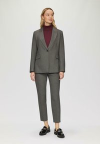 Grau maßgeschneiderter Anzug mit einem einzelnen Knopf, Spitzrevers und zwei Taschen; kombiniert mit einem bordeauxfarbenen Rollkragenpullover und schwarzen Slippern.