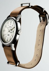 Timex Weekender kell valge diali, hõbedase korpuse, kuupäeva suurenduse ja reguleeritava pruuni nahkrihmaga, mille taust on lihtne.