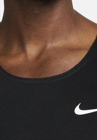 Débardeur de sport noir sans manches avec un col rond, arborant un logo Nike swoosh blanc sur la poitrine, fabriqué à partir d'un tissu lisse et extensible.