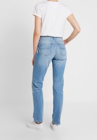 Ljusblå raka jeans med medelhög midja, bakfickor och en blekt tvätt. Matchas med en vit kortärmad skjorta och vita sneakers.