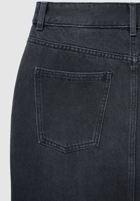 Jean en denim noir avec une taille ajustée et une poche arrière. La texture est lisse avec un motif uniforme subtil.