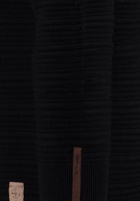 Pull en tricot noir à côtes avec un tissu texturé et une étiquette en cuir portant la marque "KEY LARGO" sur le côté.
