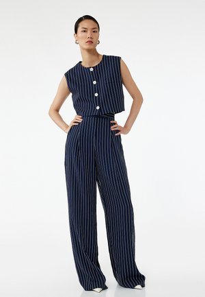 Marineblau-weiße gestreifte Zweiteiler-Set mit einem ärmellosen Oberteil mit Knöpfen und hoch taillierten, weiten Hosen. Glatte Stofftextur.