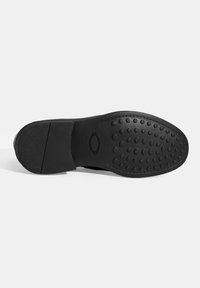 Schwarze Schuhsohle mit einer strukturierten Gummibasis, die kreisförmige Griffmuster aufweist und einen glatten Bereich in der Nähe der Ferse für Stabilität hat.