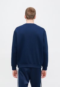 Μπλε ναυτικού φούτερ με μακριά μανίκια, ριμπ μανσέτες και τελείωμα, μονή υφή, στρογγυλή λαιμόκοψη, φορεμένο με αντίστοιχο παντελόνι με πλευρικές ρίγες.