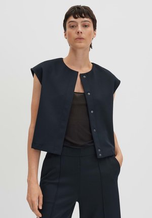 Navy cropped jacket with short sleeves, round neck, and front snap closures; paired with a black top and pants in a similar color.