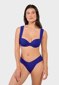 Plavi bikinijski set koji sadrži strukturiranu, podstavljenu majicu sa širokim trakama i odgovarajuće donje dijelo visokog struka, oboje od glatkog, mat materijala.