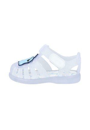 Sandal de gel transparente con diseño recortado, correa ajustable y acento en forma de mano azul en la puntera. Presenta una plantilla con patrón.