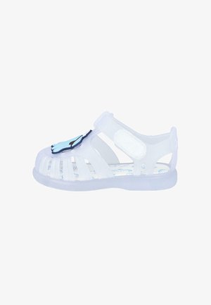Sandal de gel transparente con diseño recortado, correa ajustable y acento en forma de mano azul en la puntera. Presenta una plantilla con patrón.