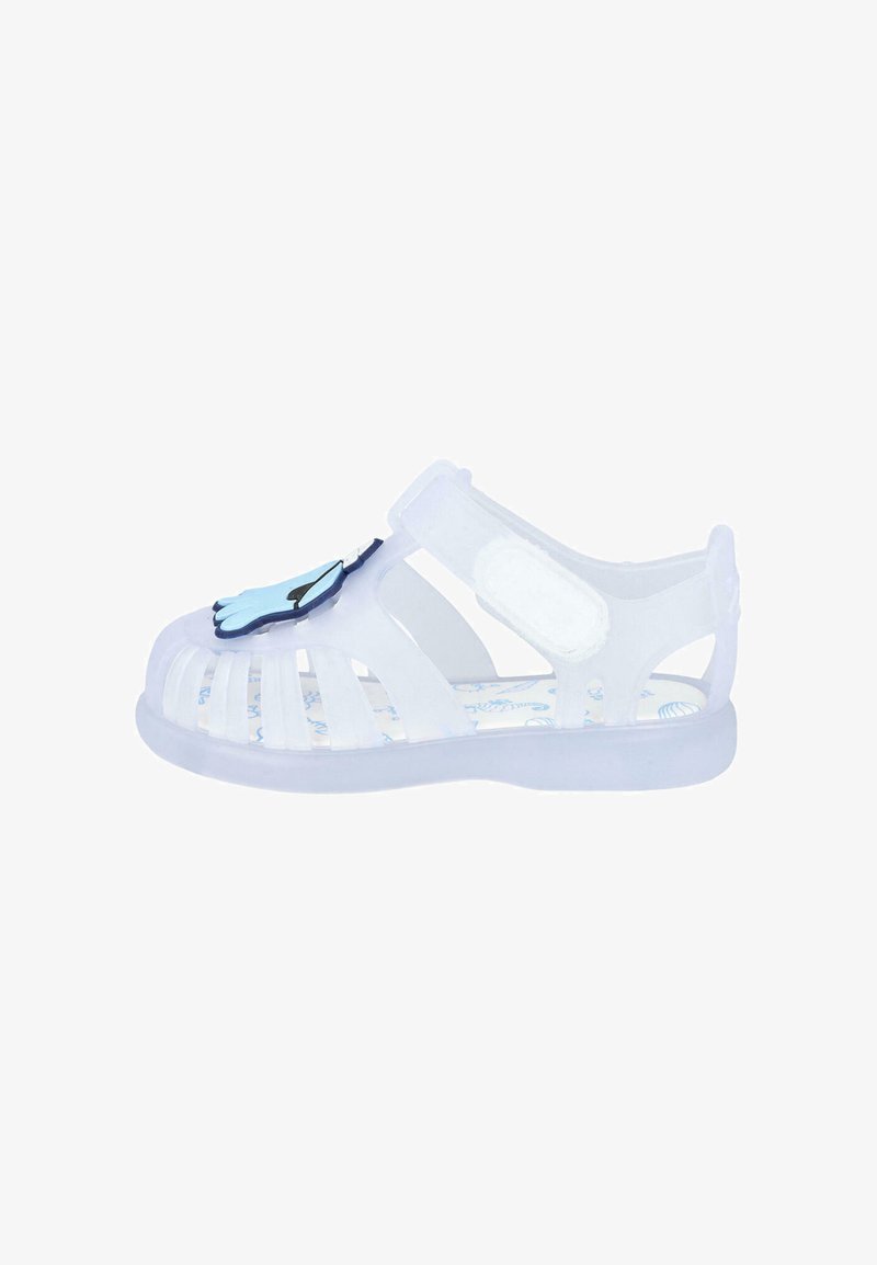 Sandal de gel transparente con diseño recortado, correa ajustable y acento en forma de mano azul en la puntera. Presenta una plantilla con patrón.