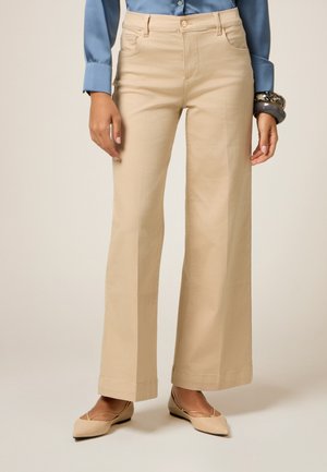 Beige weite Hose aus Baumwollmischung mit glatter Textur, Gürtelschlaufen und Seitentaschen, kombiniert mit einer blauen Bluse und beigen Ballerinas.