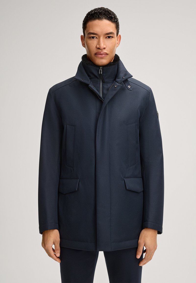 Marineblauwe jas met een staande kraag, een rits aan de voorkant en twee grote zijzakken. Glad, gestructureerd stof met een getailleerde pasvorm.