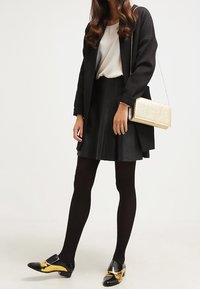 Czarny płaszcz o fakturze nałożony na białą bluzkę, zestawiony z czarną spódnicą. Dodatki to złota kopertówka. Obuwie to czarne buty ze złotymi akcentami.