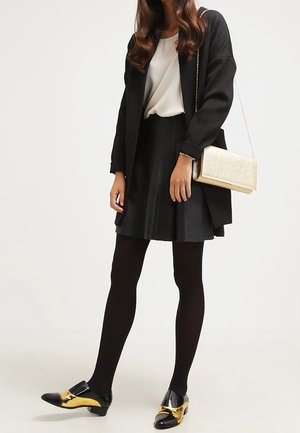 Czarny płaszcz o fakturze nałożony na białą bluzkę, zestawiony z czarną spódnicą. Dodatki to złota kopertówka. Obuwie to czarne buty ze złotymi akcentami.