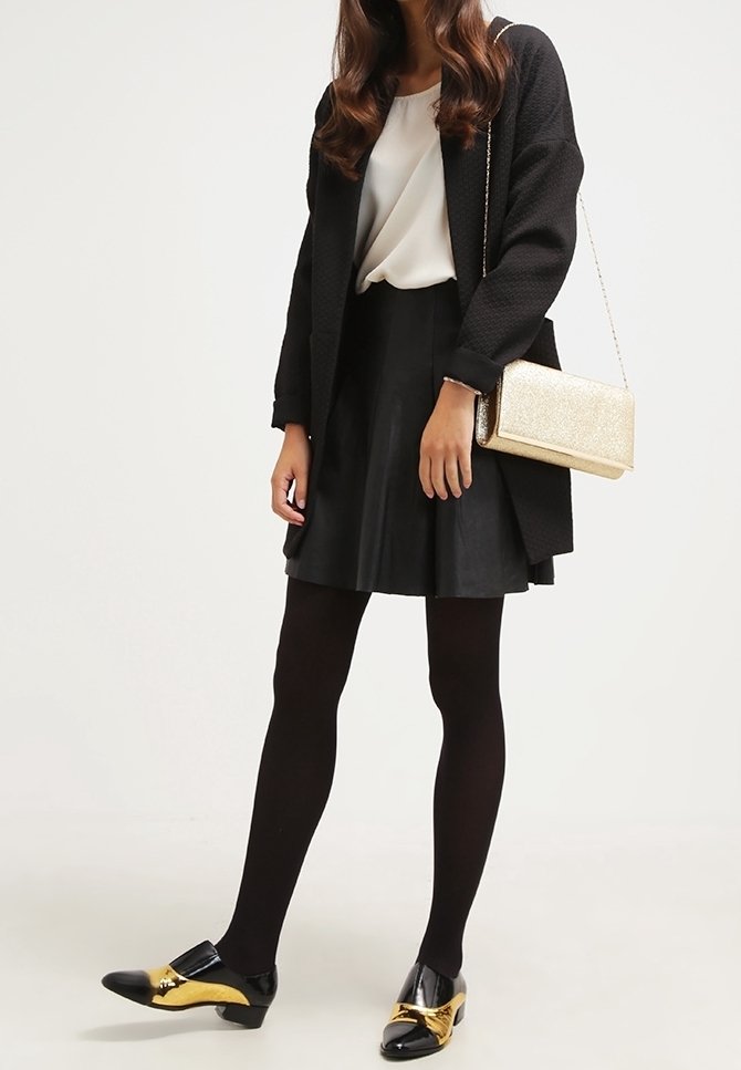 Czarny płaszcz o fakturze nałożony na białą bluzkę, zestawiony z czarną spódnicą. Dodatki to złota kopertówka. Obuwie to czarne buty ze złotymi akcentami.