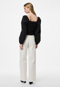 Top nero a spalla scoperta con corpetto arricciato e maniche voluminose, abbinato a pantaloni beige a vita alta e scarpe con tacco nere.