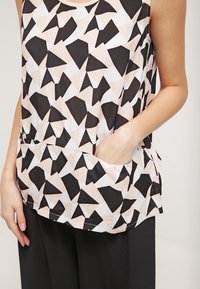 Černý, bílý a broskvový bezrukávový top s geometrickým vzorem a trojúhelníkovými tvary, s bočními kapsami. Měkký materiál, volný střih.