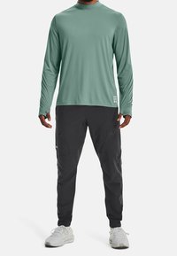 Långärmad, mintgrön skjorta med hög krage; parat med svarta byxor i cargo-stil med fickor och lös passform. Vita sneakers.