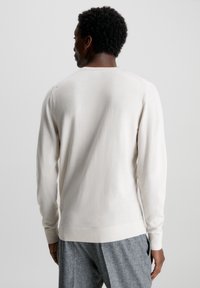 Maglione lavorato a maglia beige chiaro con maniche lunghe, scollo rotondo e polsini a coste. Texture morbida con un design aderente.