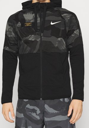 Schwarze Nike Zip-Hoodie mit camo-muster Oberteil, verstellbarem Kordelzug und Fronttaschen. Das Material hat eine strukturierte Oberfläche aus einer Mischung von Stoffen.