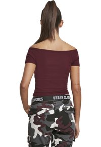 Bordová off-shoulder halenka vyrobená z žebrované látky, spárovaná s maskáčovými cargo kalhotami s logo páskem a několika kapsami.