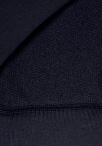 Detailní záběr tmavě námořnicky modré látky ukazující kontrastní hladké a strukturované pletené povrchy s přehnutým okrajem.