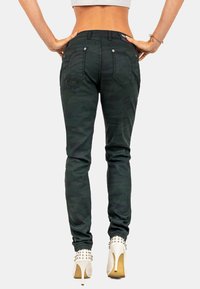 Jeans skinny in camo nero con tasche posteriori, caratterizzati da una vestibilità aderente e una trama di tessuto liscia. Indossati con tacchi bianchi borchiati.