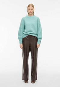 Svijetloplavi oversized pletivi pulover s okruglim izrezom, u kombinaciji s smeškim kožnim hlačama visokog struka. Smeškim cipelama upotpunjuje se cijeli outfit.