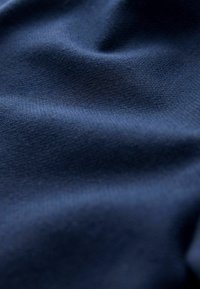 Weicher Marineblaustoff mit sichtbarer feiner Textur und sanften Falten, die Licht und Schatten reflektieren.