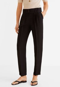 Pantalons noirs ajustés à taille haute, avec des plis et deux poches avant. Fermeture à boutons et poignets retroussés. Tissu à texture lisse.